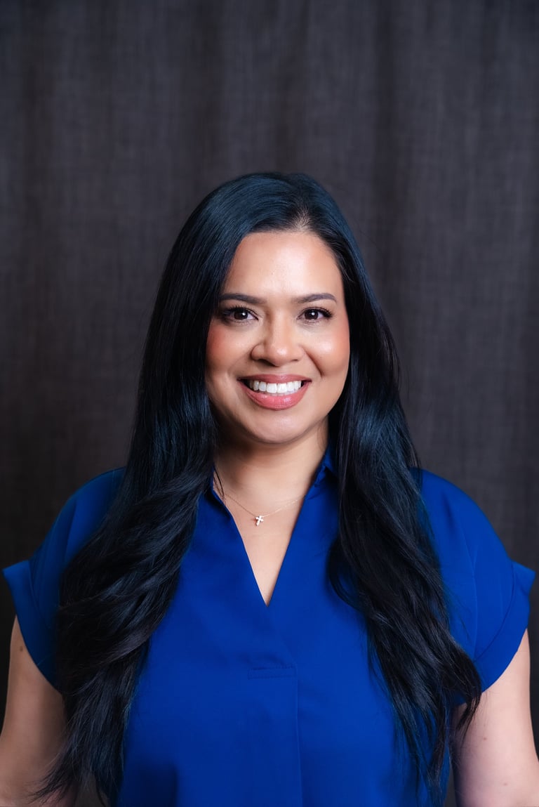 Professional headshot of a smiling woman with long black hair wearing a blue top against a dark background